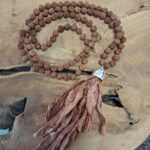 Mala in warmen Brauntönen mit Quaste auf einer Holzscheibe
